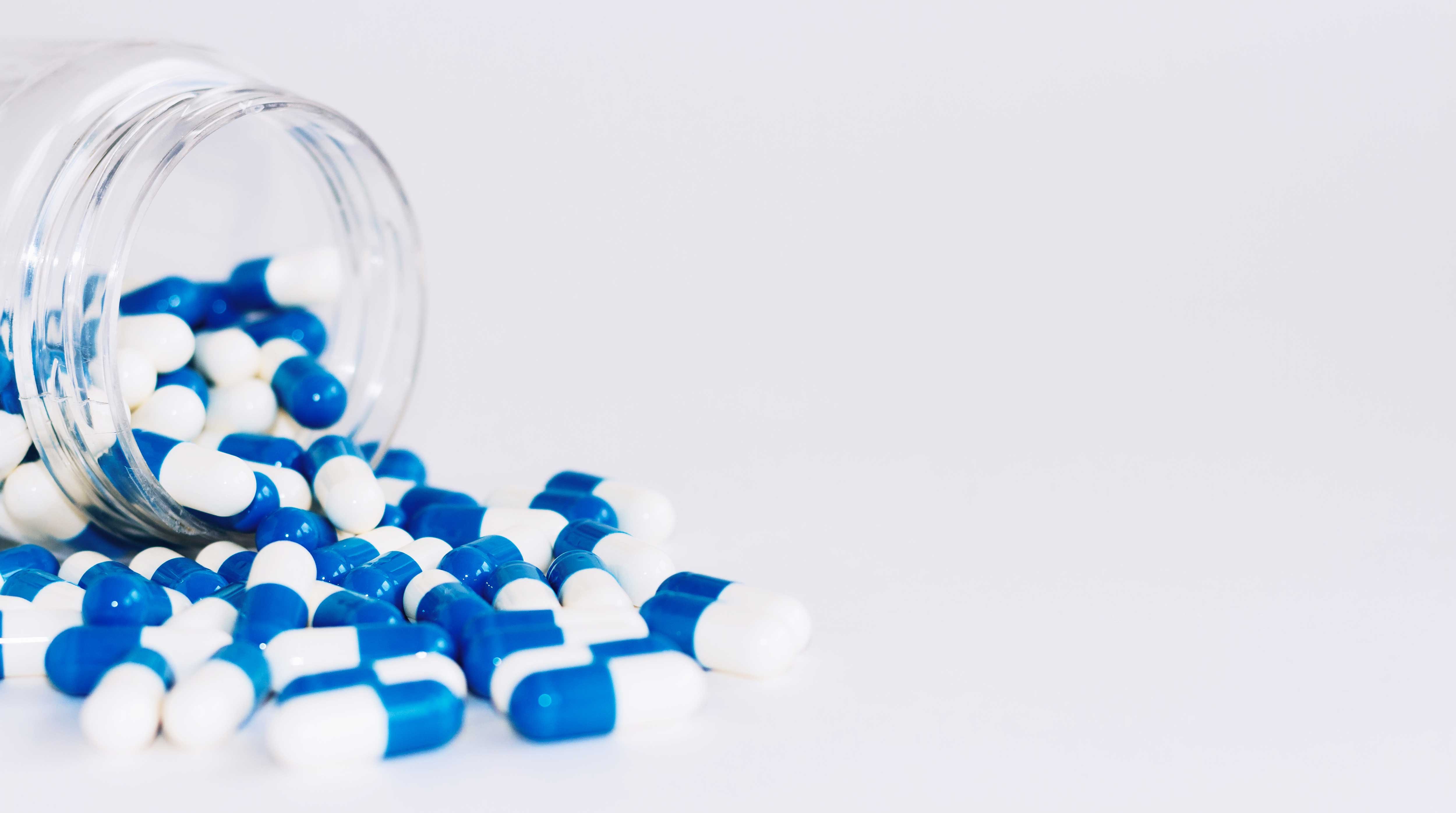 blue-white-capsules-pill-spilled-out-from-white-plastic-bottle-container-global-healthcare-concept-antibiotics-drug-resistance-antimicrobial-capsule-pills-pharmaceutical-industry-pharmacy