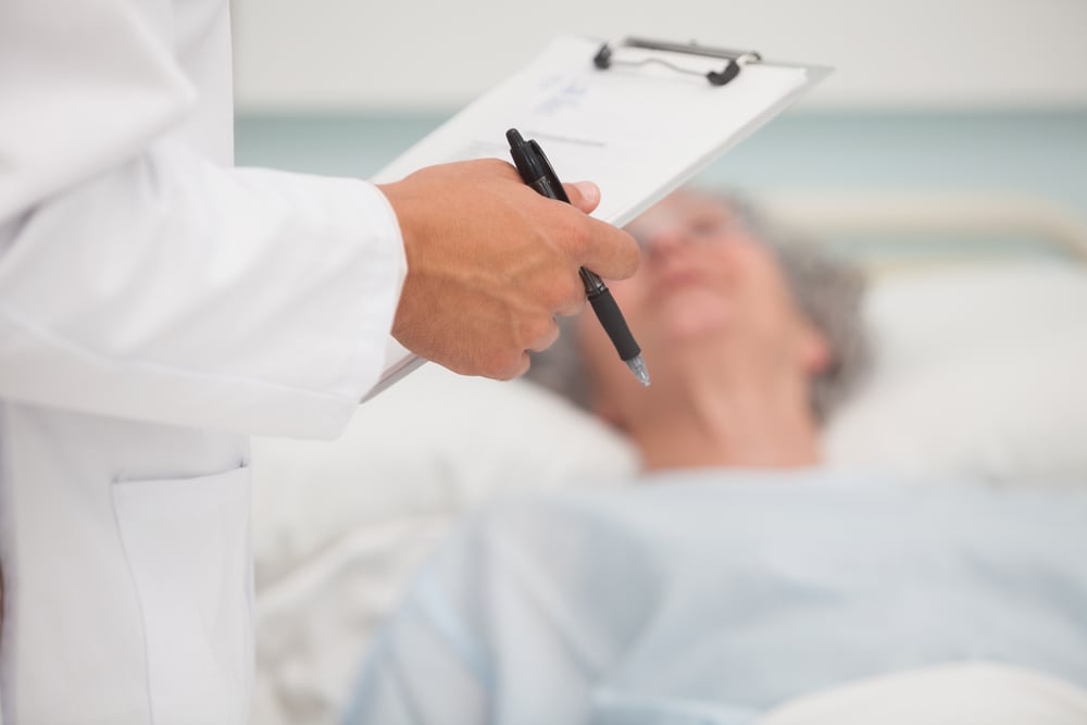 Doctor holding clipboard with elderly lady lying in hospital bed